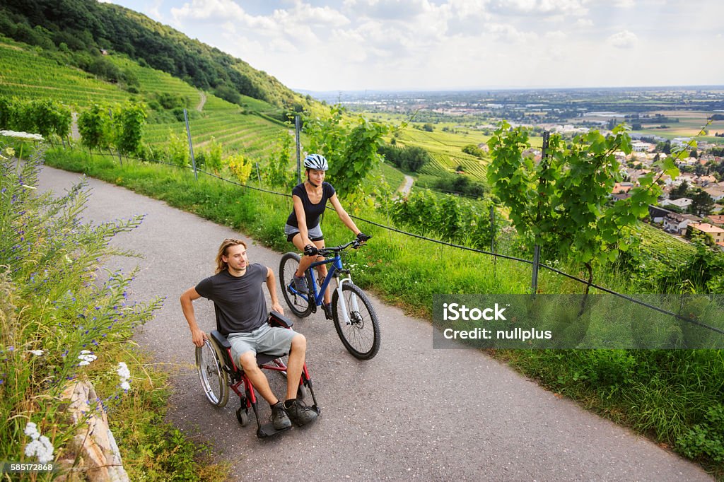 A man in a wheelchair and a cyclist share a smooth path through hillside vineyards