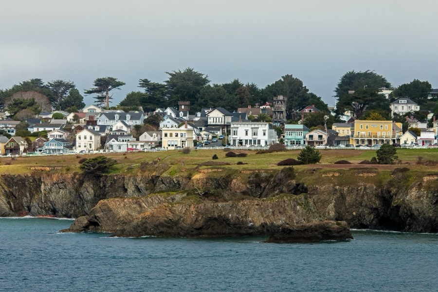 A small seaside village of white and yellow houses on a green headland above rocky cliffs